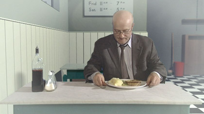 film still: “You sit in the relative peace and calm, contemplating your untouched dinner… Its virgin landscape.” 

