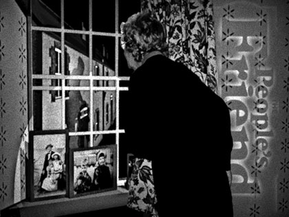 film still: People’s Friend: The woman is my brother in-law’s mother… I managed to convince her to have her picture taken during Christmas Day. Throughout the film there are bits of graphics incorporated into the pictures that help to describe the people in the village. This is my favourite, as the magazine had been a long-standing joke for me and it worked well against the ‘nosy parker’ neighbour. The scene also contains the first time I tried two features that I seem to endlessly return to: window sills with photographs, and shadows of moving people where the people don’t exist!

