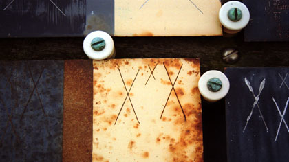 film still: XXX a: This and the next two images
are from an evolving sequence toward the end of the film. A number of a particular type of plate have been merged into each other using simple dissolves – but in ‘framed’ areas of the image. These images all contain the strong feature of (actual) overlaid _scratched crosses_. Theses are used at the site to kick-start the processes of deterioration, but for me they suggest small signatures – little identity stamps.

