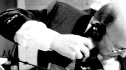 film still: Mr Budzik deals with his paperwork, seemingly finalising a deal on a Fleischermachinenfabrik (Meat Processing Machine Factory)

