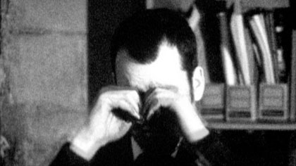 film still: Depleted by routine, he rubs at his permanently sealed eyes

